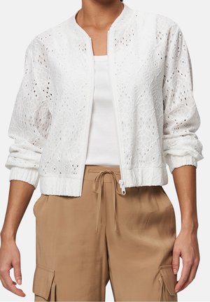 White embroidered zip-up jacket with elastic cuffs worn over a white top, paired with tan cargo pants with drawstring waist.
