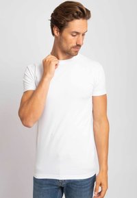 Witte bijpassende T-shirt met korte mouwen, gemaakt van katoen, met een ronde hals en een getailleerd ontwerp, gedragen met blauwe denim jeans. Soepele textuur.