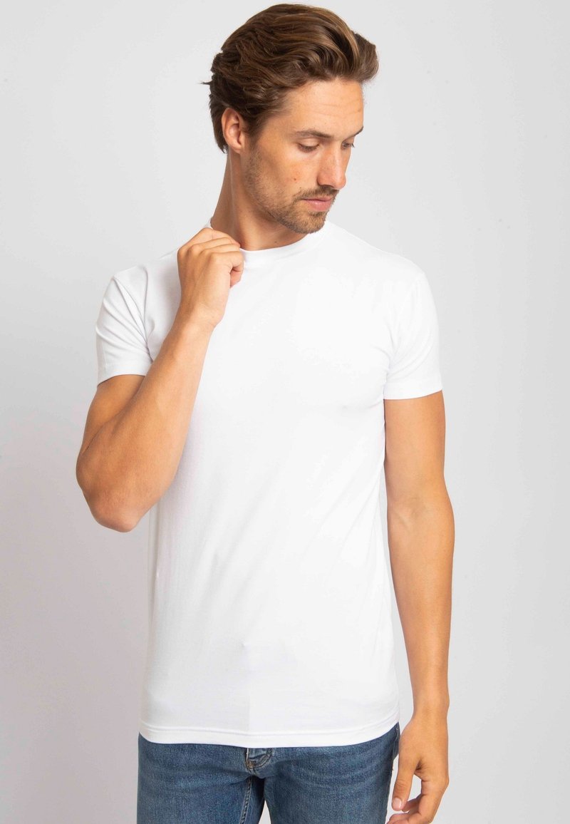 Witte bijpassende T-shirt met korte mouwen, gemaakt van katoen, met een ronde hals en een getailleerd ontwerp, gedragen met blauwe denim jeans. Soepele textuur.