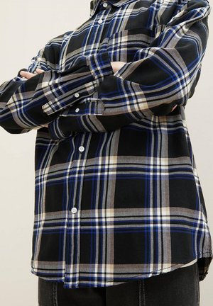Karobluse in Schwarz, Blau und Beige. Aus Baumwollmaterial, mit langen Ärmeln, variierender Streifenstärke und abgerundetem Saum.
