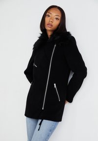 Čierny kabát s umelou kožušinou na golieri, so zipsom a bočnými vreckami. Hladký materiál, prispôsobený strih a sťahovacia časť na spodnej strane pre prispôsobenie.