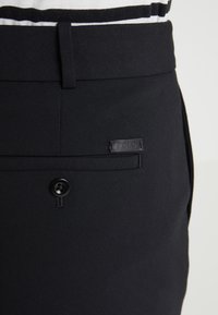 Černé kalhoty z hladké látky mají zapínání na knoflík a malou štítek "Polo" na zadním kapse.