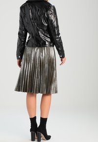 Svart, blank läderjacka kombinerad med en metallisk plisseeekjol i silvertoner, kompletterad med svarta ankelboots med klumpiga klackar.