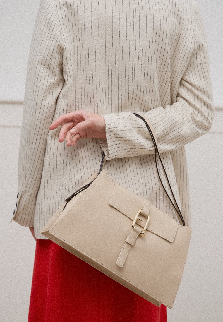 Borsa in pelle beige con un design strutturato, dotata di chiusura a fibbia e due manici neri. Posizionata su uno sfondo chiaro.