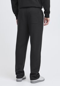 Black sweatpants made of soft fabric, featuring a back pocket and a relaxed fit. Pairs with grey athletic shoes.