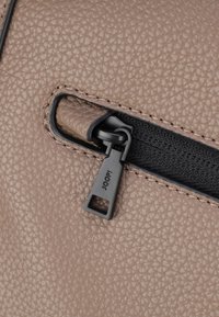 Matériau synthétique texturé beige avec une fermeture éclair noire et un tirette portant l'imprimé "JOOP!". Gros plan sur le détail de la fermeture éclair.