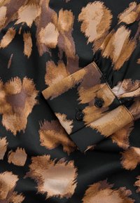Zwarte stof met bruine en beige abstracte vlekken, voorzien van een genaaid manchet met twee zwarte knopen.