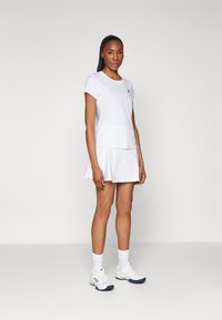 Hvid atletisk top med korte ærmer og matchende plissert nederdel. Bæres med hvide sneakers og crew-sokker. Glat, letvægtsstof.