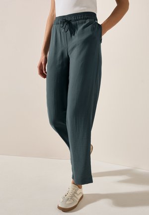 Lichte, donkerblauwe broek met een elastische tailleband, trekkoord en zijzakken, gecombineerd met beige sneakers voor een casual look.