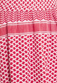 Tissu rouge et blanc avec des motifs géométriques et des rayures horizontales, présentant des sections étroitement tissées et de petites formes triangulaires.