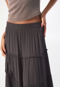 Jupe maxi à volants de couleur gris foncé en tissu léger et froissé, avec une taille élastique et de délicates coutures froncées pour plus de texture.