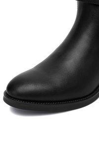 Zbliżenie na przednią część gładkiego czarnego skórzanego botka za kostkę z okrągłym noskiem i szytą podeszwą.