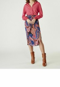 Röd knäppt blus med långa ärmar, kombinerad med en färgglad, mönstrad kjol i blått, rosa och brunt, med en sidoklyfta. Bruna anklarstövlar.