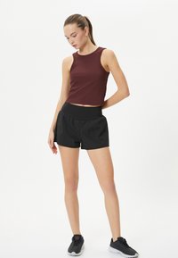 Burgundy ärmlös crop top som matchas med svarta träningsshorts. Toppen har en figursydd design, medan shortsen har ett elastiskt midjeband.