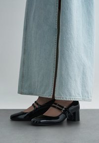 Schwarze Mary-Jane-Pumps aus Lackleder mit doppelten Riemen, getragen zu hellblauen, weit geschnittenen Jeanshosen.