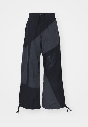 Zwarte en grijze windbreakerbroeken met een relaxte pasvorm, elastische tailleband, trekkoorden en een geometrisch paneelontwerp.