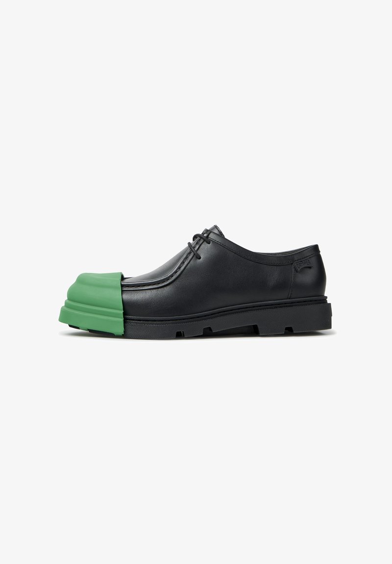 Chaussure habillée en cuir noir à lacets avec embout en caoutchouc vert épais et semelle noire épaisse, vue de côté isolée sur fond blanc.