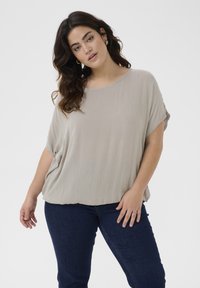 Top corto de color gris claro, con un corte relajado, tejido sutilmente texturizado y escote redondo. Combinado con jeans de color azul oscuro.