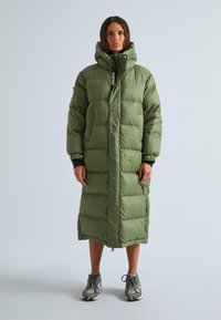 Garšs, pūkains zaļš mētelis ar kapuci, ar ievelkamiem priekšējiem kabatām, divām sānu kabatām un elastīgām aprocēm. Nēsāts pār tumšu apģērbu un sporta apaviem.