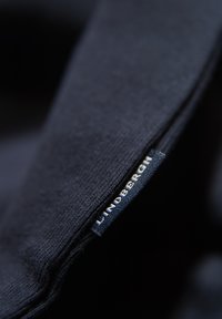 Granatowy materiał o miękkiej fakturze, z widoczną etykietą "LINDSBERGH". Zbliżenie podkreśla szczegóły materiału i szwów.