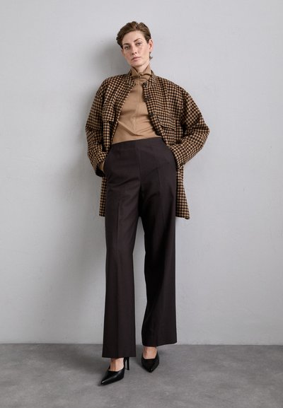 Braunes Houndstooth-overgroßes Sakko, beiger taillierter Rollkragenpullover, schwarze weit geschnittene Hose und spitze schwarze Absätze. Glatte Texturen mit einem strukturierten Look.
