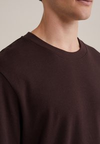 Sudadera de algodón marrón con cuello redondo y una textura suave, que presenta un diseño sencillo y un corte relajado. No hay patrones ni acentos visibles.