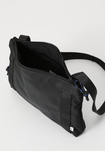Sort nylon skuldertaske med lynlås, flad form, justerbar rem og teksturerede detaljer. Åben top afslører indersiden.