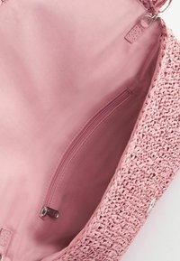 Intérieur de sac à main tissé rose avec une poche en tissu zippée et une fermeture à fermoir métallique sur le bord d’ouverture.