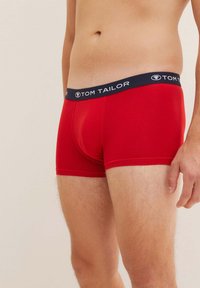 Rote Boxershorts aus einem weichen Material mit einem navyfarbenen Bund, der das weiße Branding "TOM TAILOR" trägt. Die Shorts enden auf Oberschenkelhöhe.