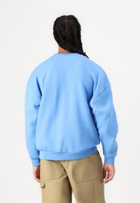 Világoskék, laza szabású pulóver, bordás mandzsettákkal és aljjal, puha tapintású anyaggal, ejtett vállakkal. Bézs cargo nadrággal párosítva.