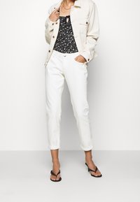 Cream denim jacket with brown buttons, paired with a black floral top featuring a tie front, and white cropped pants. Black heeled sandals.