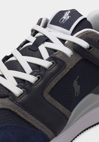 Μπλε ναυτικό και γκρι αθλητικό παπούτσι με λευκά κορδόνια, πάνελ από δέρμα και δίχτυ, και κεντημένο λογότυπο παίκτη πολο στη πλευρά και τη γλώσσα.