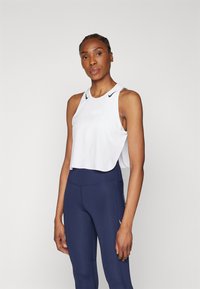 Hvid ærmeløs crop top med rund halsudskæring og sort logo detalje, parret med marineblå høj talje leggings med søm.