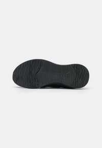 Semelle extérieure de chaussure de sport noire avec surface texturée, présentant un motif en forme de vague pour l'adhérence et un détail central moulé du logo.