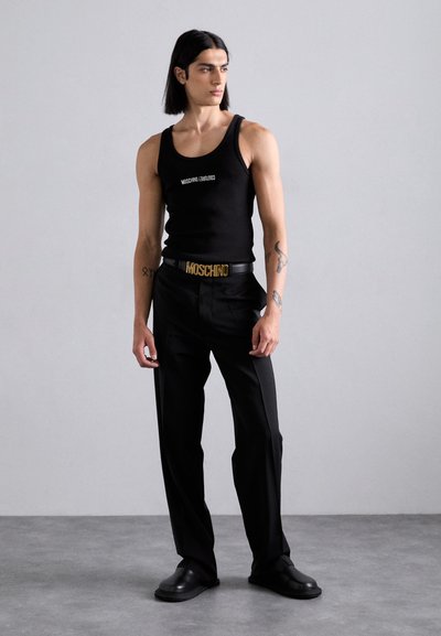 Melnā bezgriezuma blūze ar baltu Moschino tekstu, apvienota ar melnām, brīvām biksēm un melnu jostu ar zelta Moschino sprādzi. Melnas kurpes.