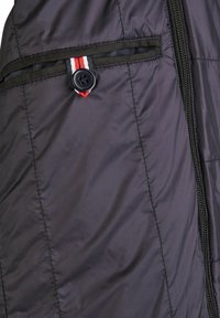 Padded jakna od tamnoljubičastog najlona. Ima patentni zatvarač, bočnu džepu s trakama u crvenoj, bijeloj i plavoj boji, te detalj s gumbom.