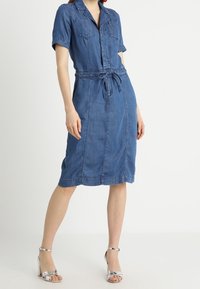 Abito camicia in denim con maniche corte, cintura alta, tasche anteriori e lunghezza a metà polpaccio. Colore blu con una texture liscia e design classico.