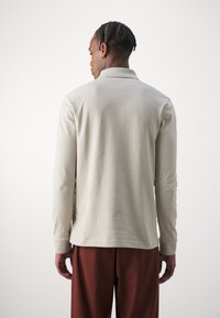 Langærmet polo shirt i lys beige bomuld, med krave og knaplukning, parret med mørkerøde bukser. Glat tekstur og tætsiddende design.