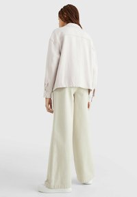 Light pink, textured oversized jacket with a collar and buttoned cuffs, paired with wide-leg cream pants and white sneakers.