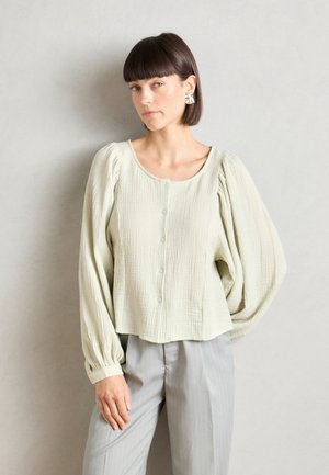 Lichtgroene, gestructureerde blouse met lange mouwen, een ronde halslijn en knoopsluiting. Gecombineerd met grijze pantalon met streepjesmotief.