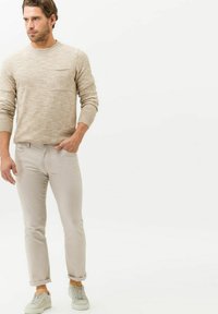 Light beige knit sweater with a crew neck and a breast pocket, paired with light-colored rolled-up pants and gray sneakers.