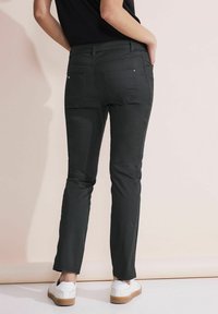 Pantalones negros ajustados de cintura media, con bolsillos delanteros y traseros, textura suave y diseño hasta el tobillo, combinados con zapatos blancos.