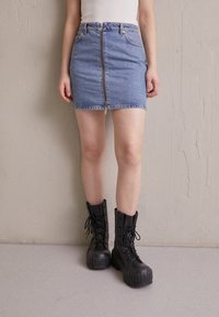 Denim mini kjol med framdragkedja, två sidofickor och rå kant, i kombination med kraftiga svarta snörkängor.