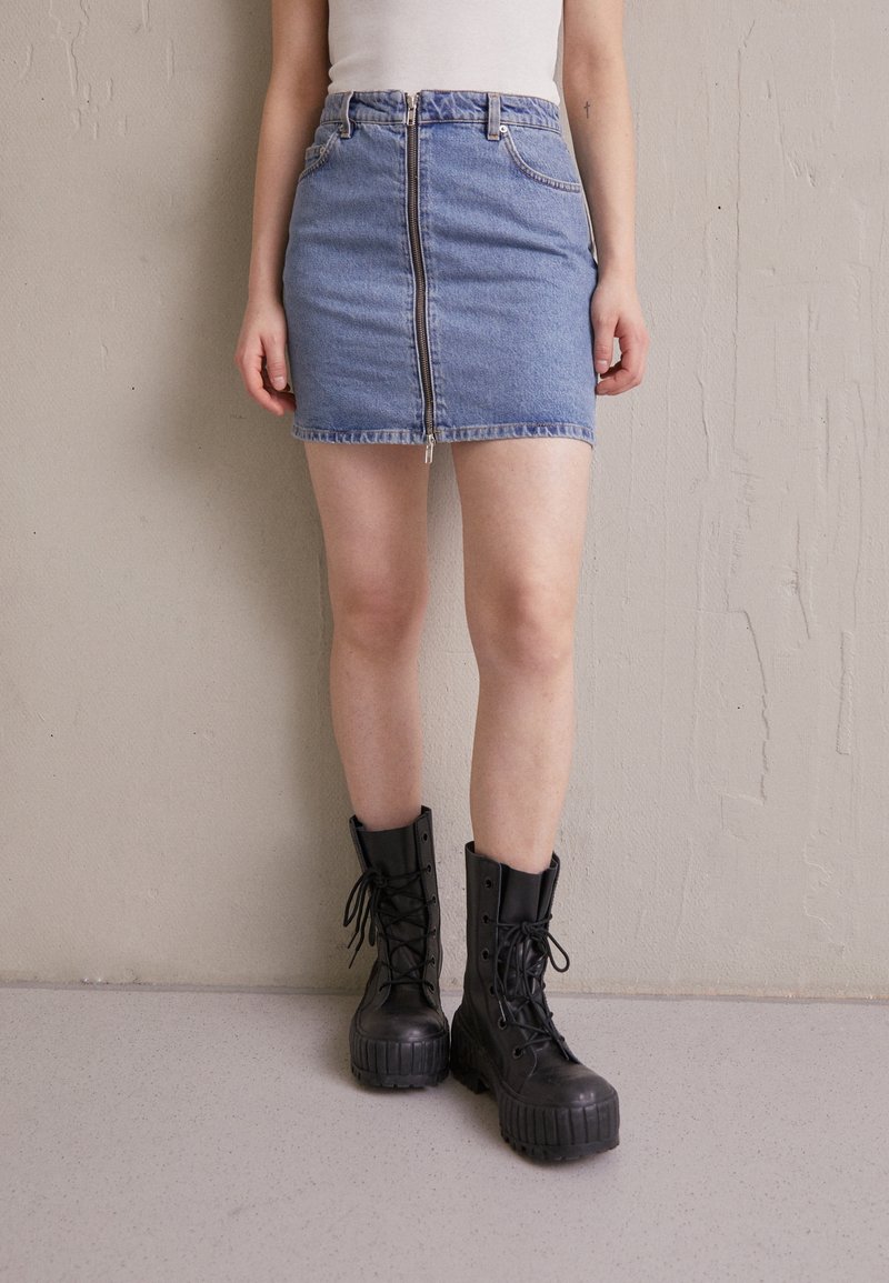 Denim mini kjol med framdragkedja, två sidofickor och rå kant, i kombination med kraftiga svarta snörkängor.