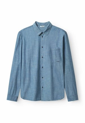 Lichtblauwe langharige blouse van chambray stof, met een borstzak en contrasterende donkere knopen.