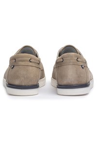 Scarpe in suede di un beige chiaro con due occhielli per i lacci, suola in gomma bianca e un sottile accento blu sul retro. Texture complessiva liscia.