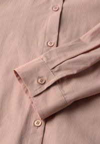 Chemise rose clair à manches longues avec des poignets à boutons et des boutons assortis le long de la patte de boutonnage.