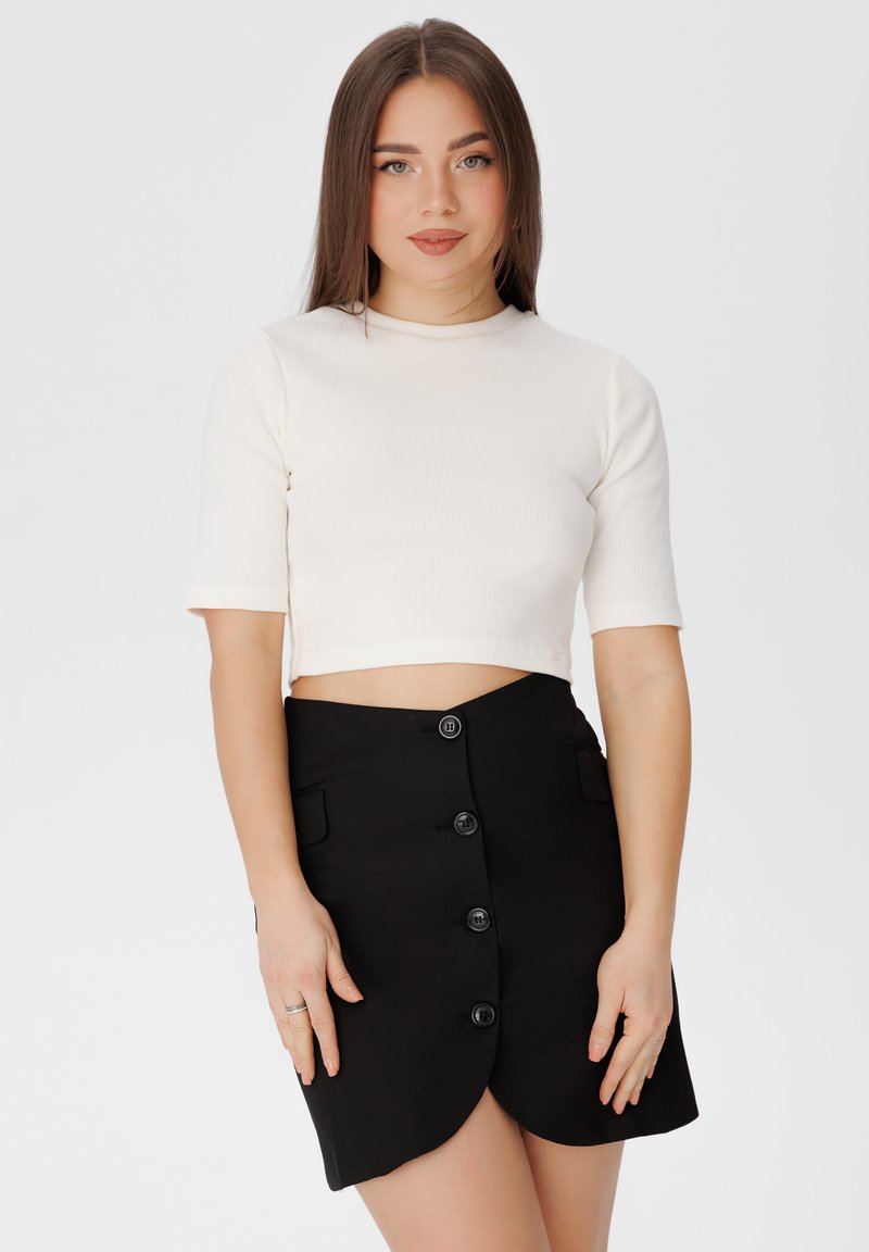 Bílý žebrovaný crop top s krátkým rukávem doplněný černou sukní vysokého pasu s vykrojeným lemem a šesti černými knoflíky.