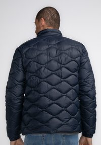 Dunkelblauer gepolsterter Mantel mit einem gesteppten Wellenmuster, hohem Kragen und elastischen Bündchen, aus glänzendem, glattem Material gefertigt.