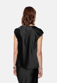 Top in satin nero con maniche corte, texture liscia, scollatura arrotondata e vestibilità ampia, visto da dietro.